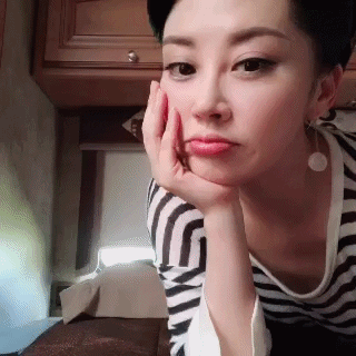 图片中的她穿着黑白条纹上衣,梳着利落的短发,单手扶脸,害羞地低下头.