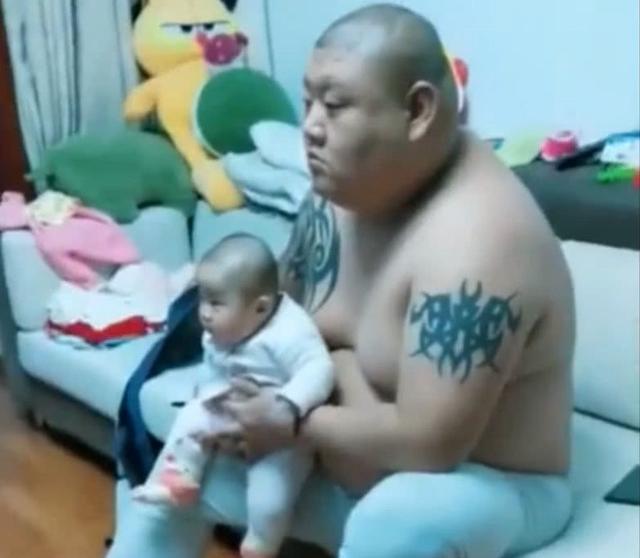 爸爸抱着宝宝一起看电视，长相神情完全同步，遗传基因太强大了